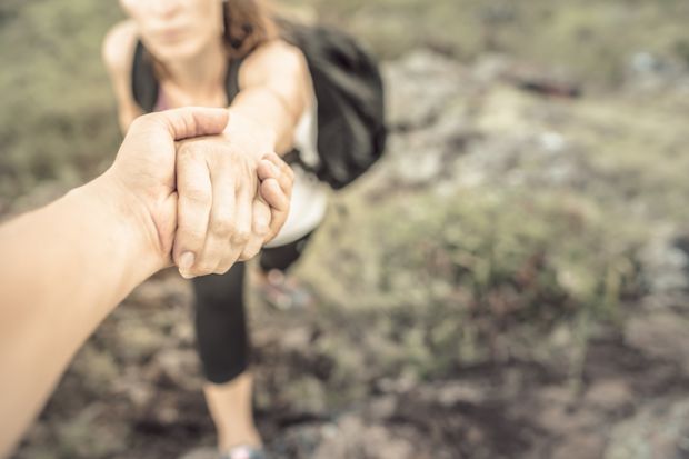 Hikers helping each other climb up mountain