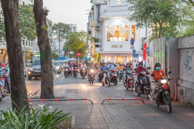 Ho Chi Minh City, Vietnam - January 9, 2019 a crowd of motorbikes drives along the pedestrian crossing and continue driving along the sidewalk in spite of roadblocks.