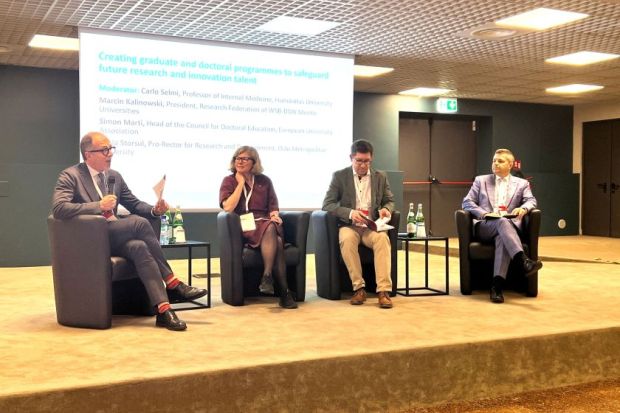 Four panelists sitting on couches on a stage in front of a screen at the THE Europe summit