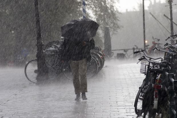 Someone with an umbrella walks through heavy rain past some bicycles