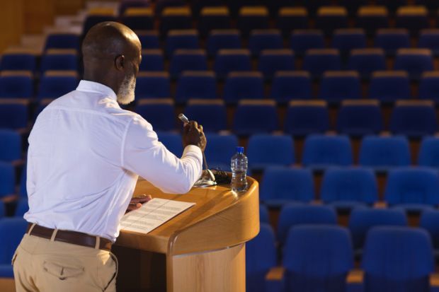 A man at a lecturn with a mic in front of an empty auditorium