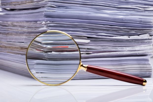 Close-up Of Magnifying Glass On Background Of Stacked Paper Files
