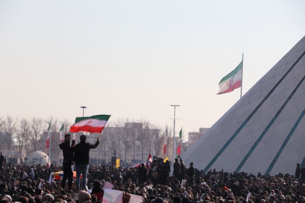 Two men holding Iranian flag beside Azadi Tower
