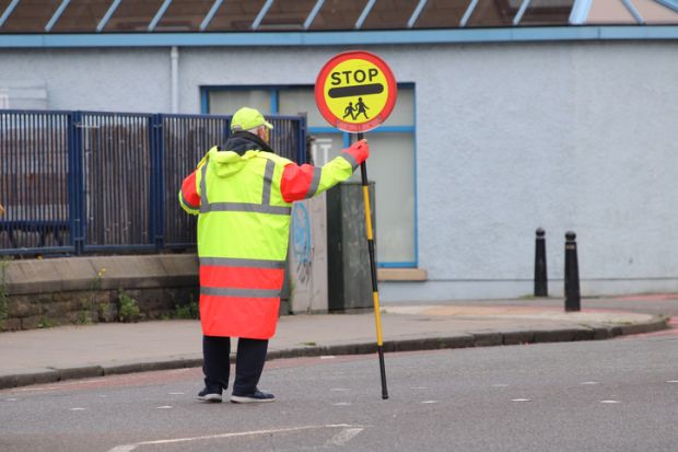 Lollipop man standing in the middle of a pedestrian street crossing near a school at pick up time