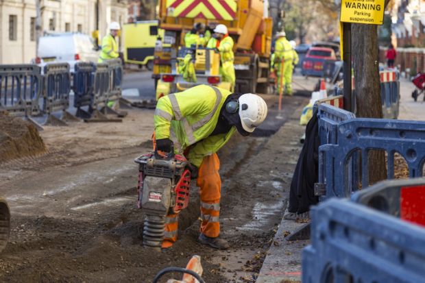 Man in yellow vest drilling the pavement in a London Street.