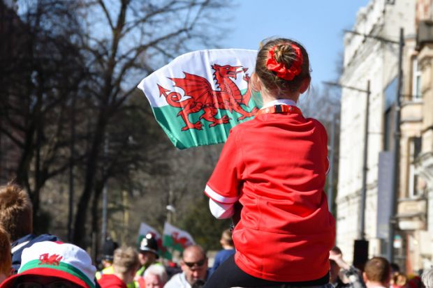 Young girl on father’s shoulders waving a Welsh flag.