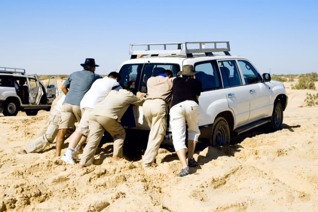 People pushing car stuck in sand