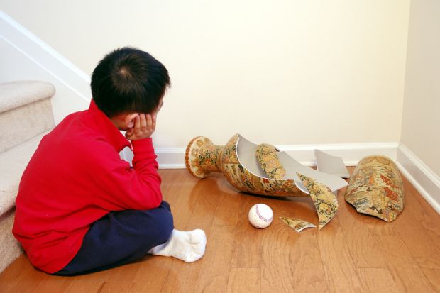 A young boy contemplates a smashed vase, with a ball sitting next to it A young boy contemplates a smashed vase, with a ball sitting next to it