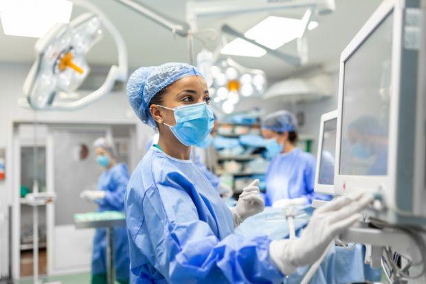 Anesthetist Working In Operating Theatre Wearing Protecive Gear checking monitors.