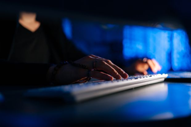 man working typing on keyboard laptop computer sitting at desk in dark room