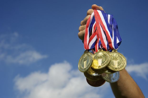 A hand holding a clutch of gold medals