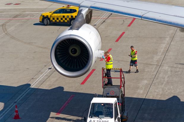 Airport technician doing maintenance work at jet engine of Edelweiss Air Airbus A340-300 HB-JMC airplane on a sunny summer day.