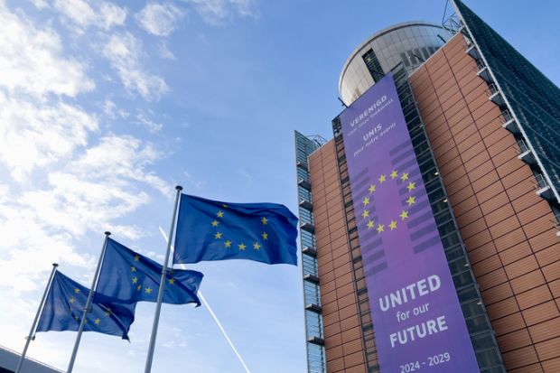 Several EU flags and the exterior view of the European Commission headquarters in Brussels,