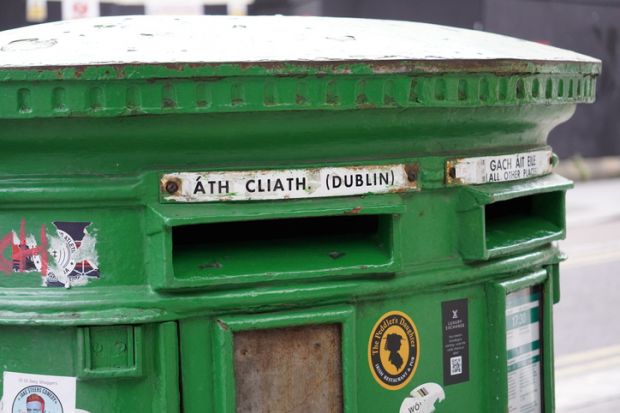 A close-up of a traditional green Irish post box in Dublin, with its distinctive Gaelic and English text