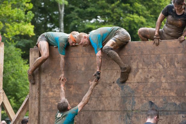 Team of people help each other tackle a high slippery wooden barrier on their gruelling 12 mile assault course