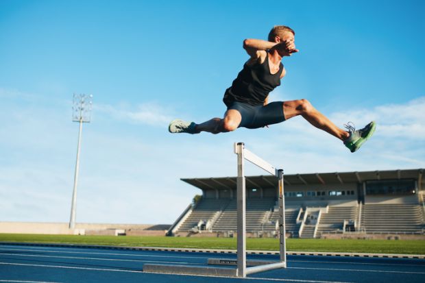 oung athlete jumping over a hurdle during training on racetrack in athletics stadium. oung athlete jumping over a hurdle during training on racetrack in athletics stadium.