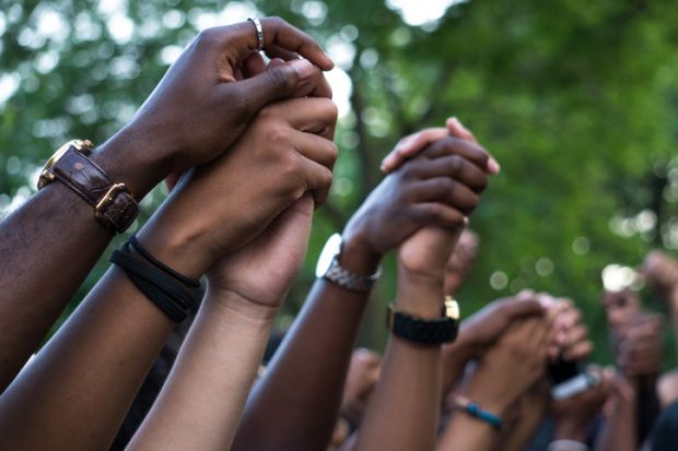 Interlocked hands at a Black Lives Matter protest. BAME academics are facing dual pandemics of Covid and racism.