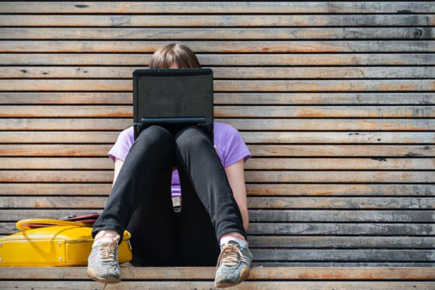 woman using a small black laptop on a bench