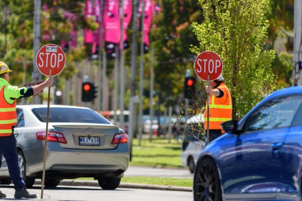 Two traffic control workers are holding stop signs to stop the traffic at a roundabou Two traffic control workers are holding stop signs to stop the traffic at a roundabout