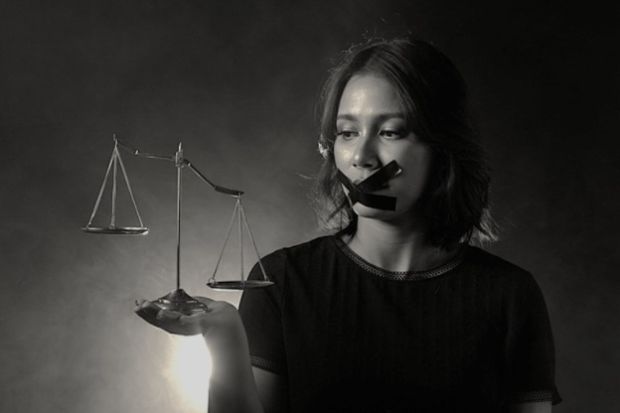 A woman wide tape over her mouth holds uneven scales of justice
