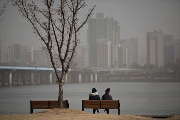 Two people sit on a bench before the Han River and Seoul city skyline
