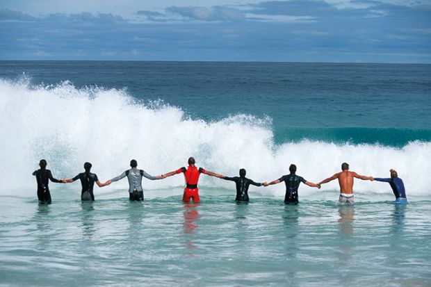 A line of people holding hands facing a wave