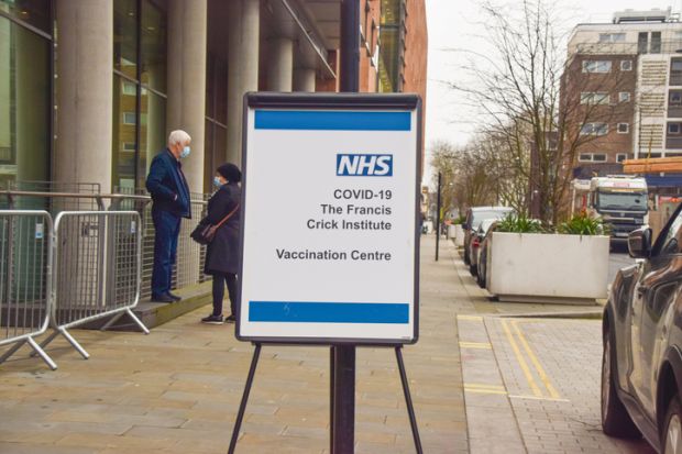 London, United Kingdom - February 1 2021 People with protective face masks stand next to a COVID-19 Vaccination Centre sign at the Francis Crick Institute in St Pancras.