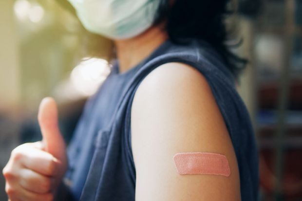 lose-up adhesive bandage on unrecognized person's arm after injection of vaccine, people in face mask received a coronavirus COVID-19 vaccine and giving thumb up to recommended inoculation