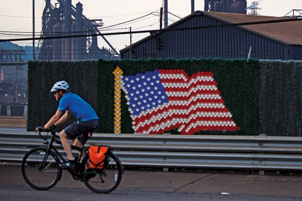 Man riding bicycle past United States of America flag