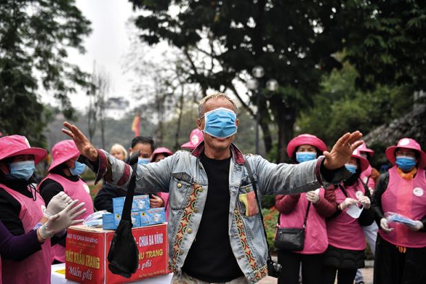 Man with medical mask over eyes surrounded by a crowd of people