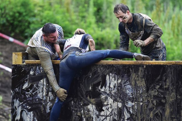 Men helping woman to climb obstacle