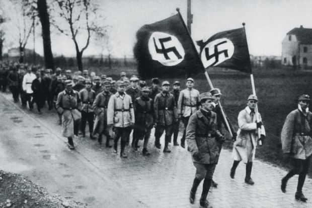 Men marching behind flags with swastikas on them