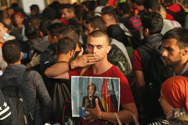 A migrant from Syria holds a picture of Angela Merkel