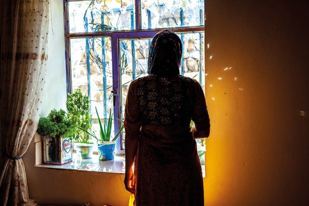 Iranian Kurdish woman who was circumcised at eight stands in silhouette by a window