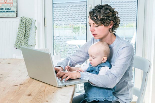 Mother working on laptop in kitchen with baby