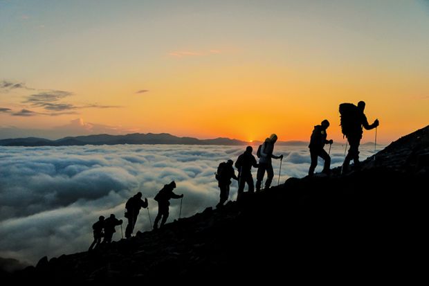 people climbing mountain with mist below