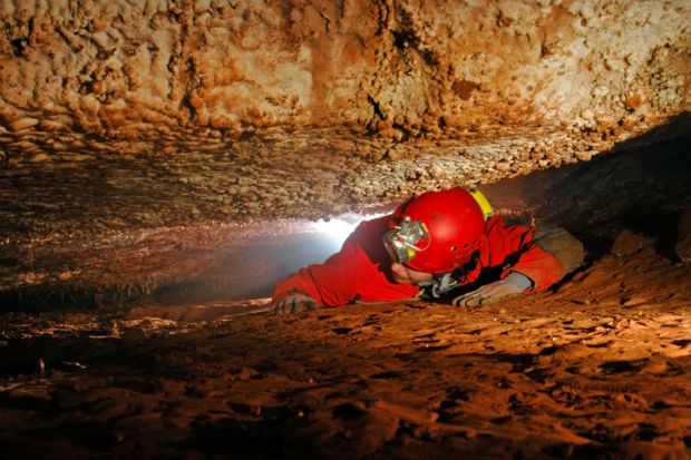 Man crawling through a narrow cave