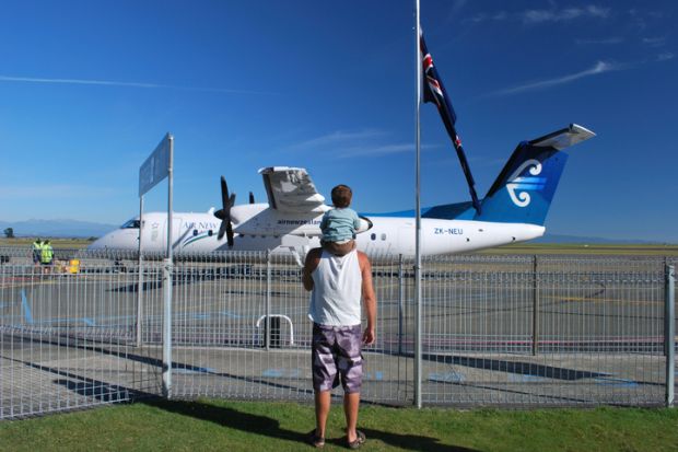 Nelson, New Zealand - March 10, 2012. A Man with a Boy on his shoulders look out to an Air New Zealand Aeroplane at Nelson's Domestic Airport, Nelson Region, New Zealand.