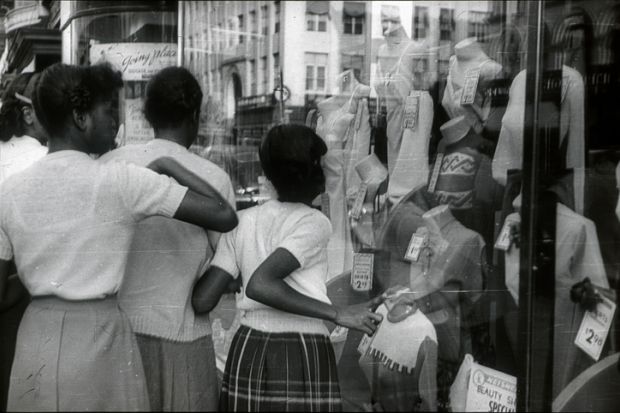 New York City, NYS, USA, 1951. Afro-American teenagers in front of a shop window in Harlem. They look at the offers of a fashion store.
