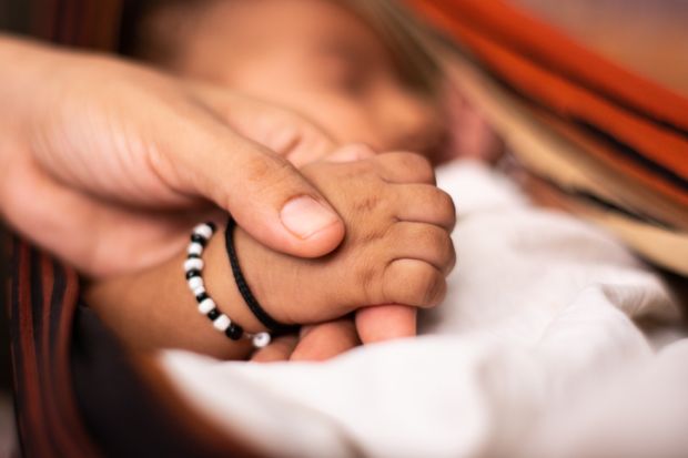 newborn baby holding the parent hand while sleeping at cradle