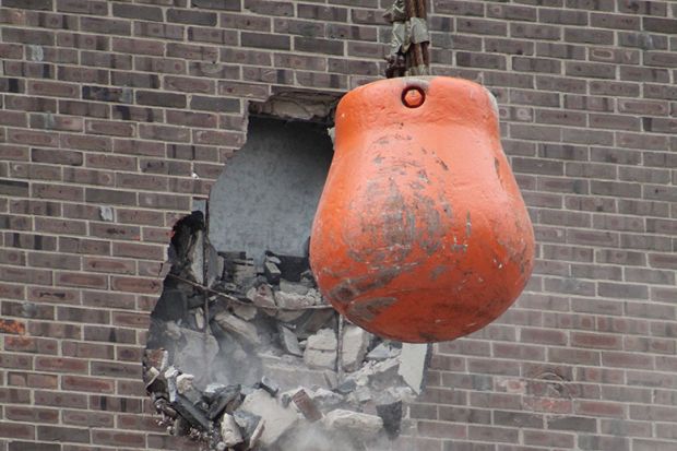 Orange wrecking ball demolishing building wall