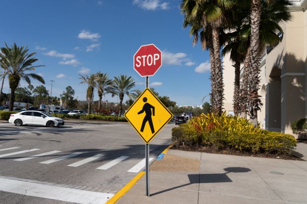 Orlando, Florida, USA - January 20, 2022 A stop sign with a Pedestrian Crossing Sign outside a shopping mall is shown in Orlando, Florida, USA.