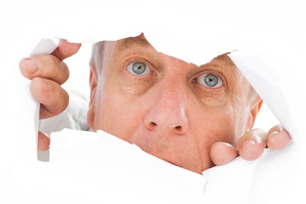Man peeks through tear in paper