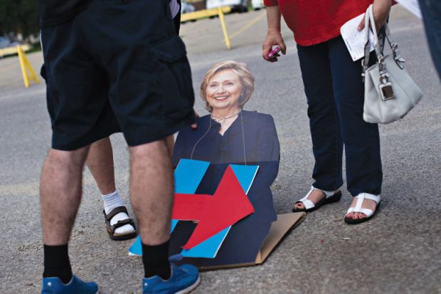 People looking at cardboard cutout of Hillary Clinton lying on road