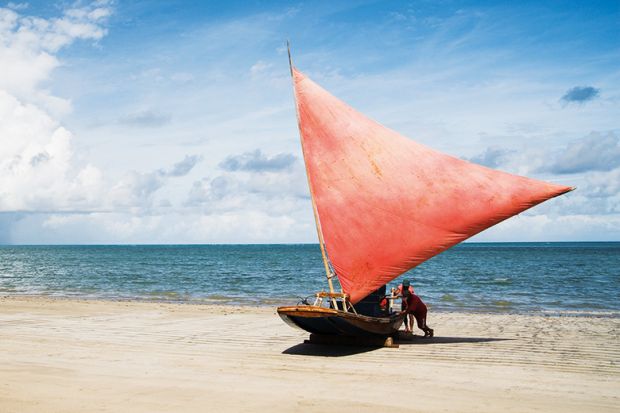 People pushing sailboat from sea onto beach People pushing sailboat from sea onto beach