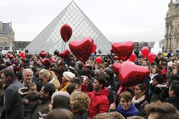 People with red heart balloons outside the Louvre