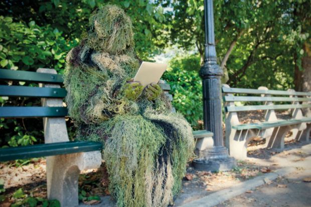 Person in ghillie suit reading on bench