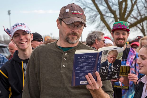 A man reads a Donald Trump book while waiting in a long line for admission to a Trump campaign rally, 2016. To illustrate that academics might need to 'tread carefully' with courses on Trump.