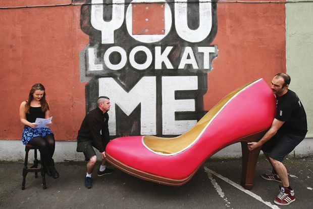 Two men carrying a big red shoe while a young woman sits reading Two men carrying a big red shoe while a young woman sits reading