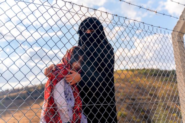 A refugee mother and her child behind a migrant camp fence A refugee mother and her child behind a migrant camp fence